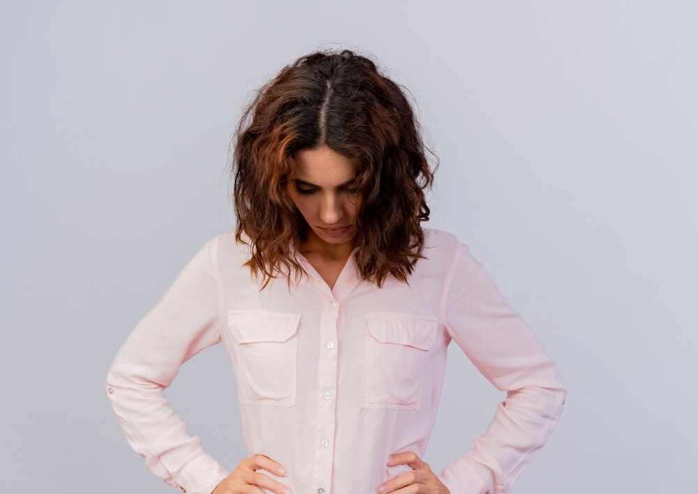 Disappointed young caucasian woman puts hands on waist looking down