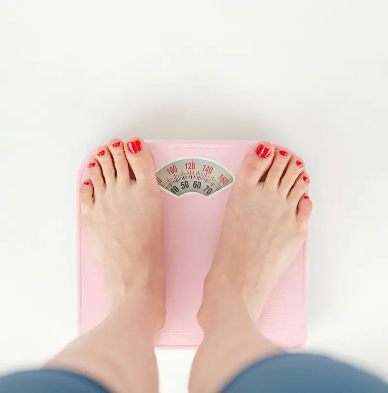 Top view of crop anonymous barefoot female measuring weight on scales on white background